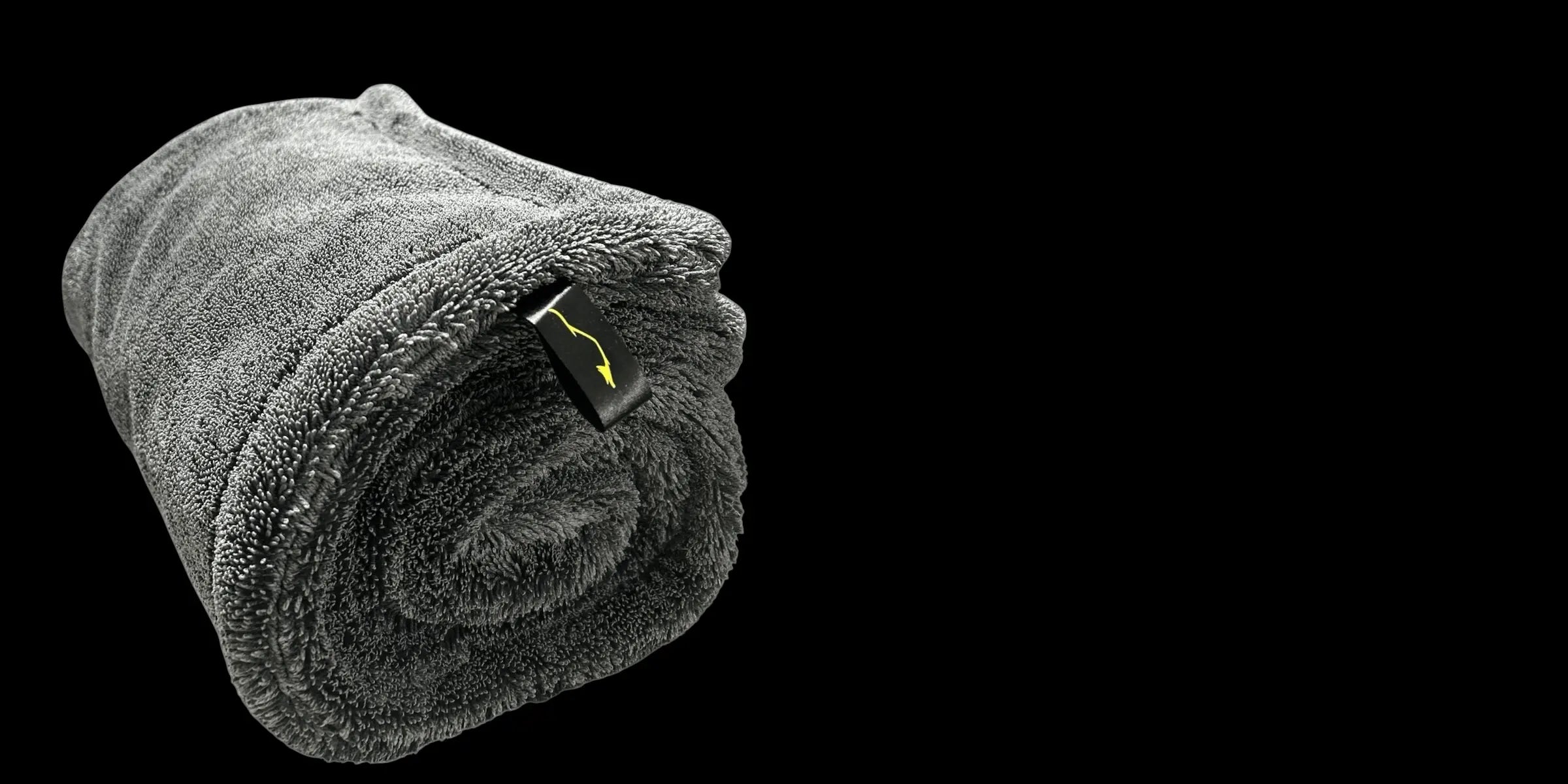 Sleek Dudes Max Dry 2K microfiber drying towel, rolled, against a black background