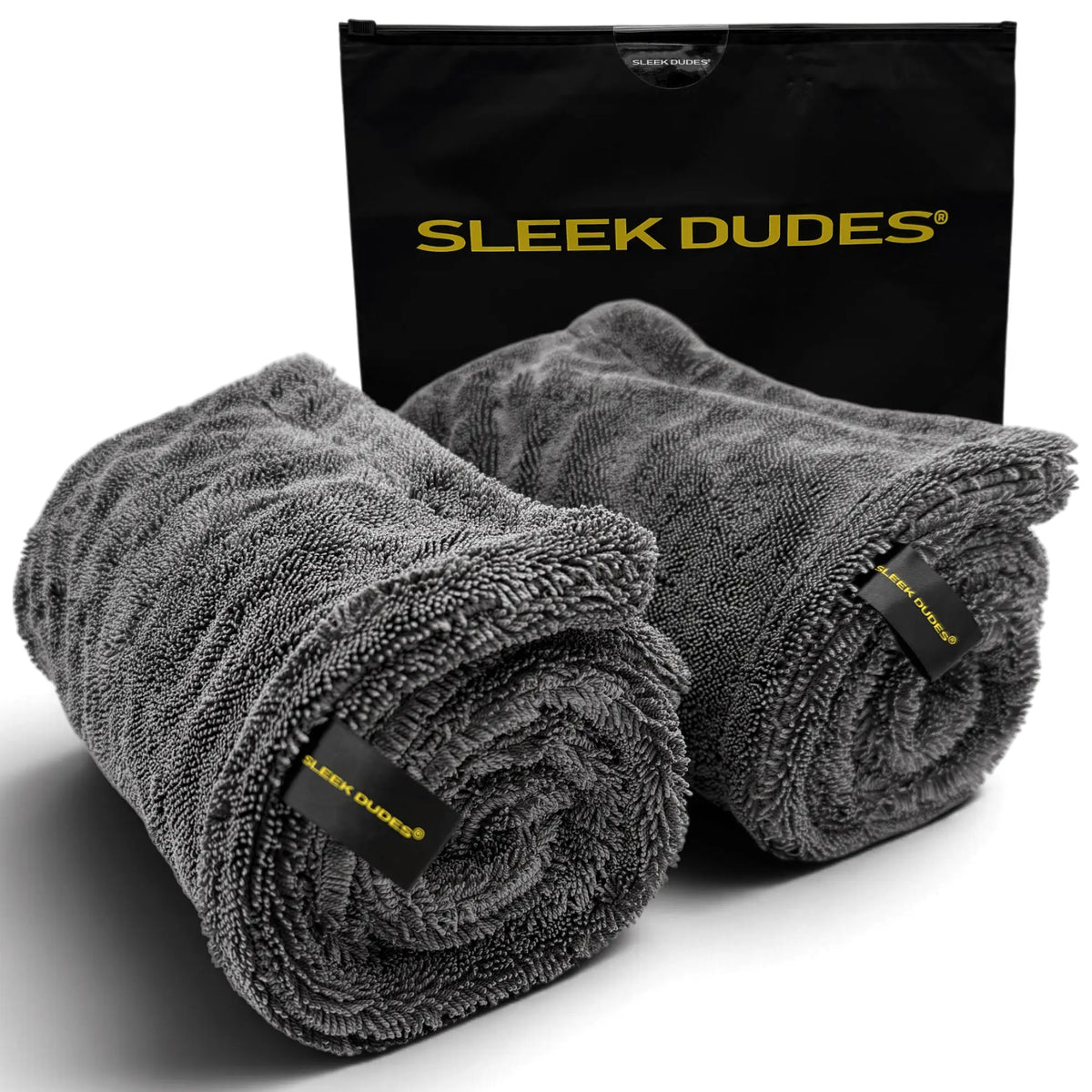 Two rolled dark gray microfiber towels with black and yellow SLEEK DUDES labels, displayed in front of a black SLEEK DUDES carrying bag on a white background.