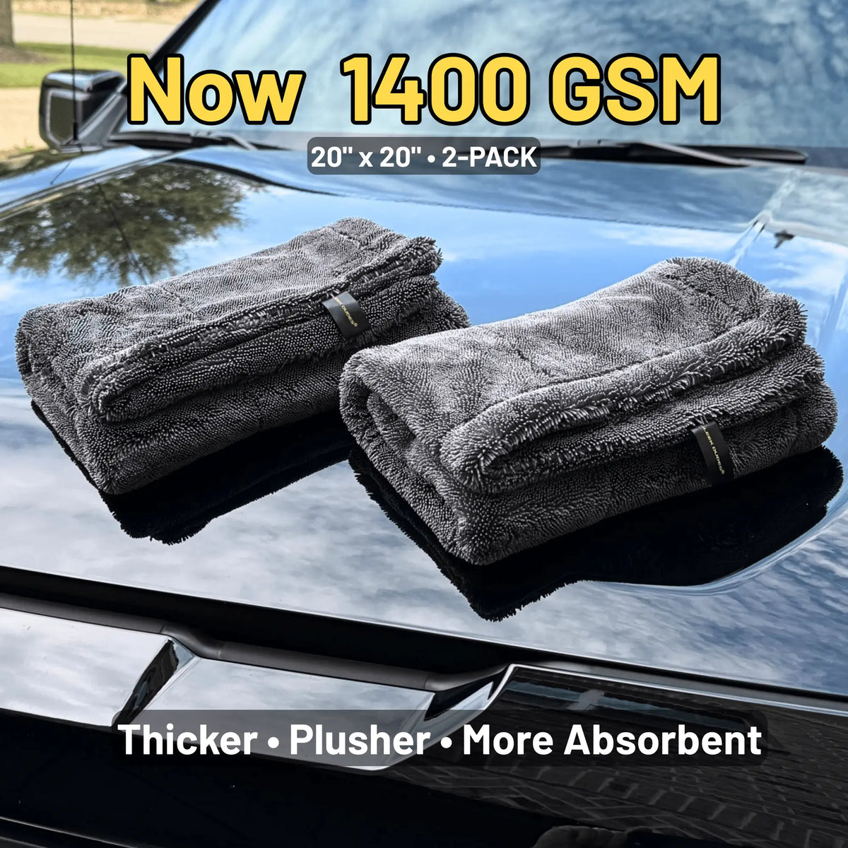Two folded dark gray microfiber cloths displayed on a glossy black car hood, with promotional text reading 'Now 1400 GSM', '20" x 20" - 2-PACK', and 'Thicker • Plusher • More Absorbent'.
