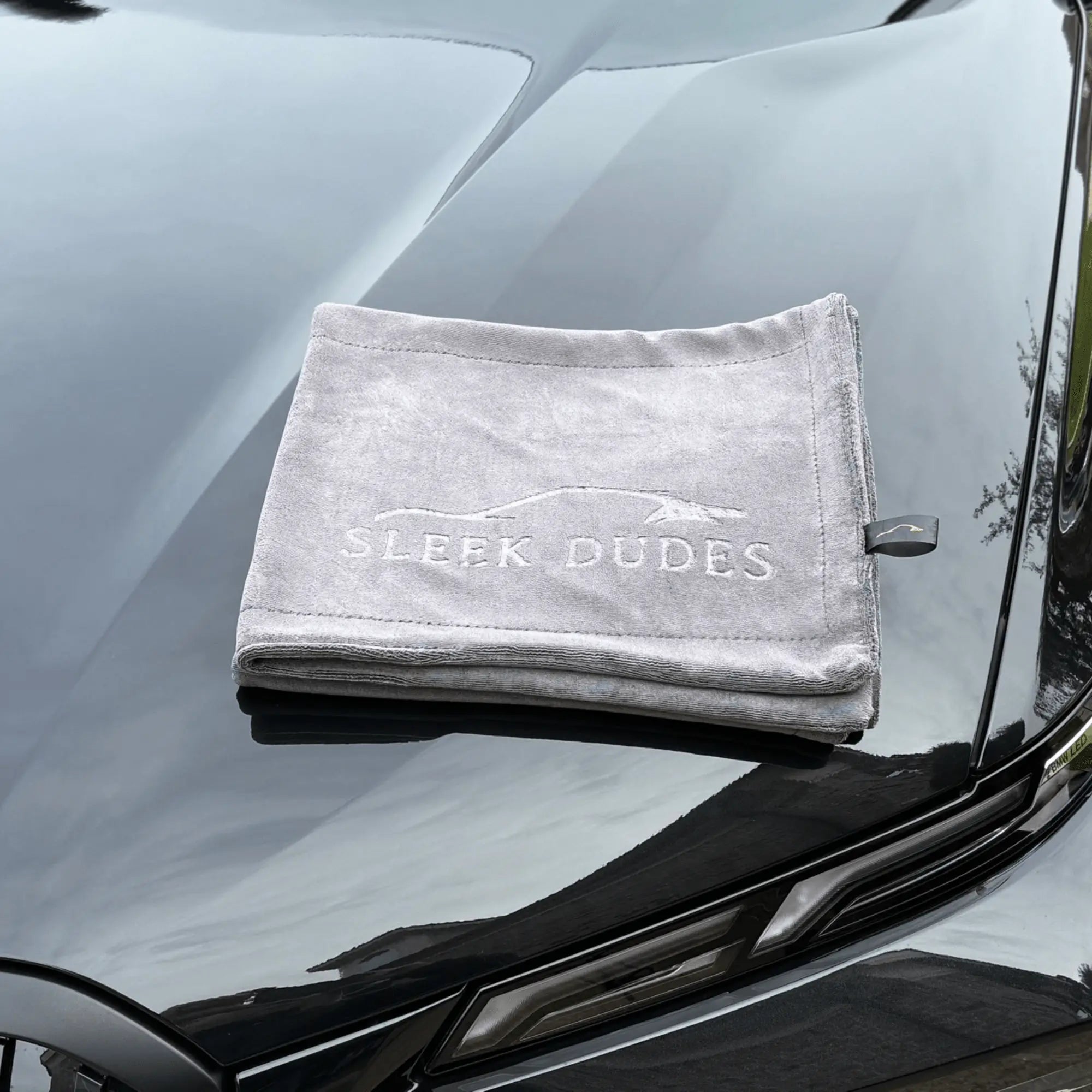 Gray towel with 'Sleek Dudes' branding on a car's hood