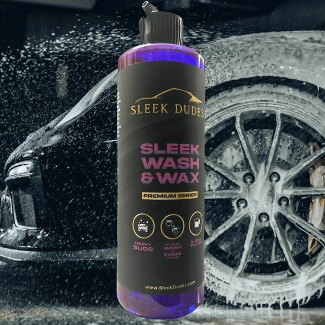 Bottle of Sleek Dudes Sleek Wash & Wax car shampoo in front of a foamy wheel, showcasing its heavy suds and wash-and-wax formula for premium car detailing.