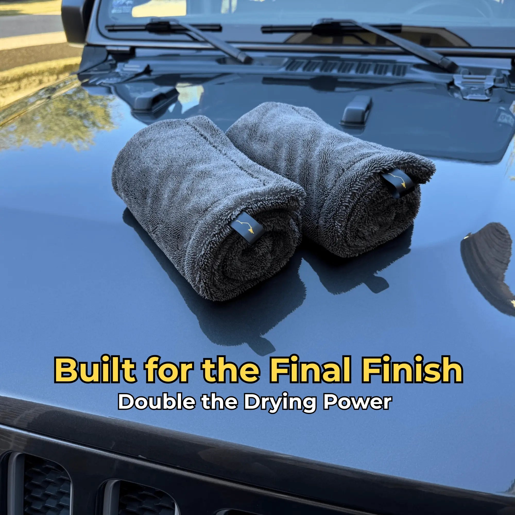 Two rolled-up towels on a car hood with text 'Built for the Final Finish Double the Drying Power' on a reflective car surface.
