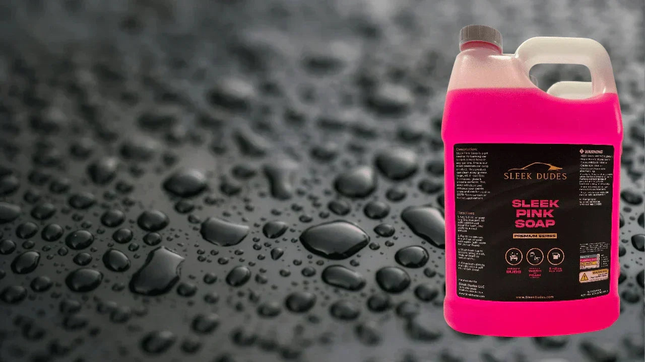 One-gallon container of Sleek Dudes Sleek Pink Soap shown in front of a close-up background of water beads on a black car panel, emphasizing its premium pH-neutral, high-foaming car wash formula.
