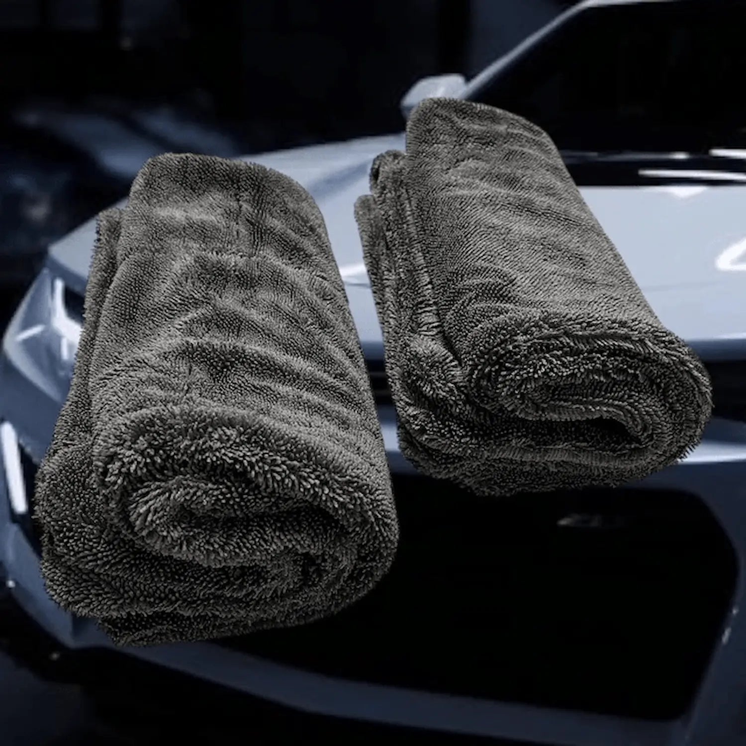 2 rolled microfiber car drying towels – Double Trouble by Sleek Dudes – in front of a white car.
