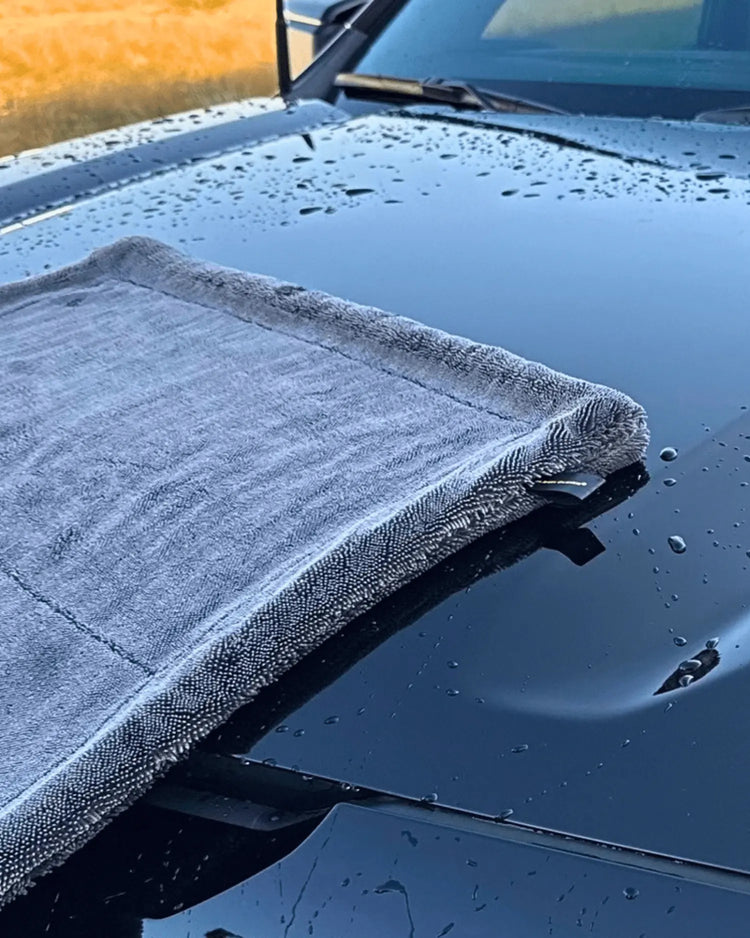 A gray microfiber car wash cloth draped over the hood of a wet black vehicle outdoors.