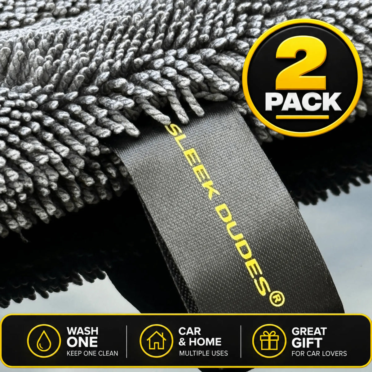 Two gray microfiber car wash towels shown close-up with a black fabric loop tag printed with the brand name 'SLEEK DUDES' in yellow. A circular badge at the top right says '2 PACK', and a black informational strip at the bottom lists features: 'WASH ONE', 'CAR & HOME MULTIPLE USES', and 'GREAT GIFT FOR CAR LOVERS'.