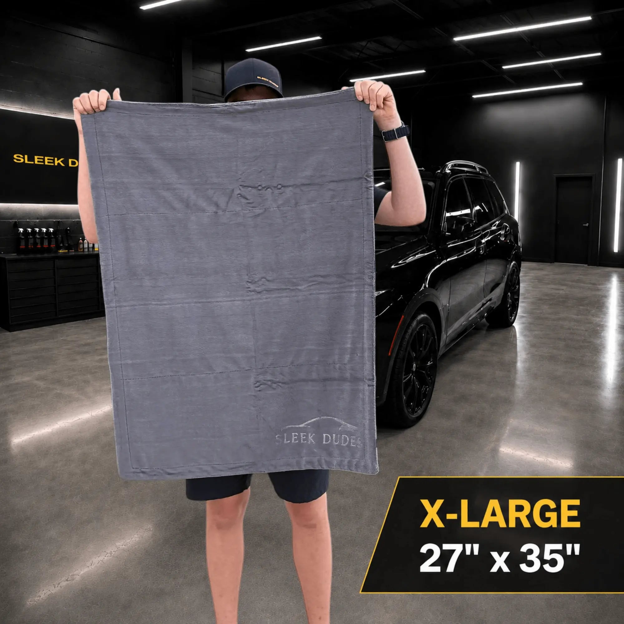 Person holding a large gray towel with 'Sleek Dude' branding in a garage setting.