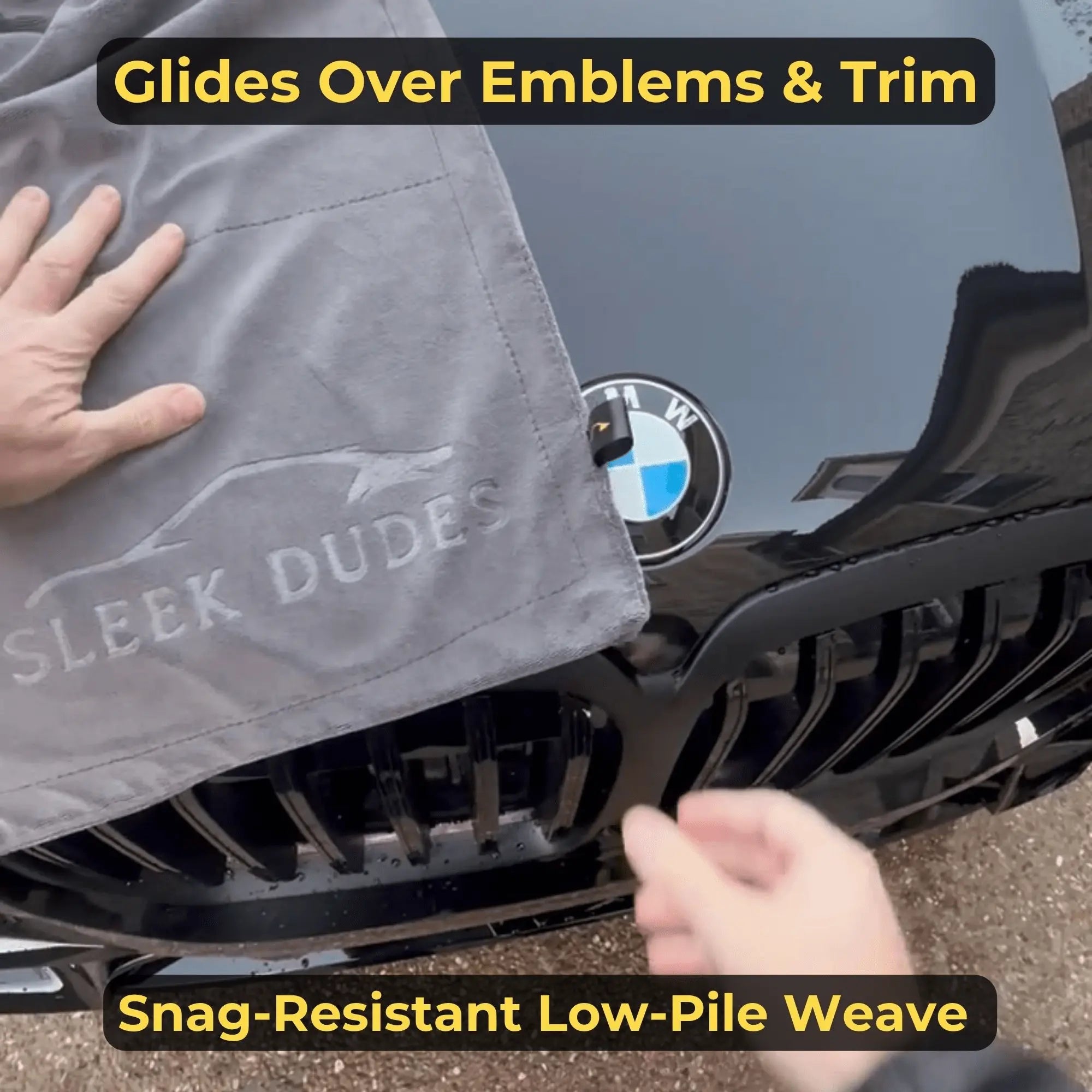 Person using a gray towel labeled 'Sleek Dudes' to clean a BMW emblem and trim.