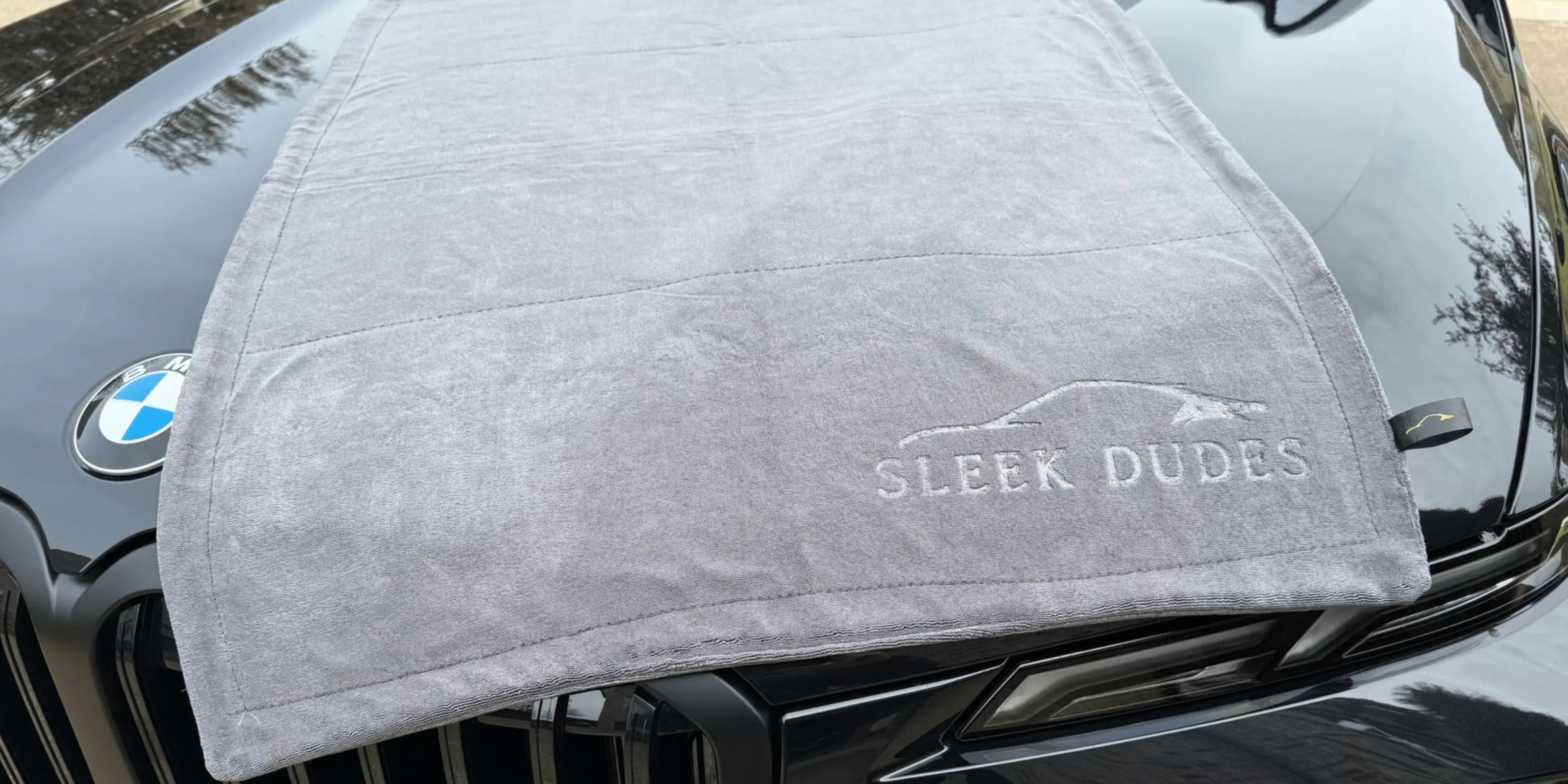 Gray towel with 'Sleek Dudes' branding draped over a car's hood