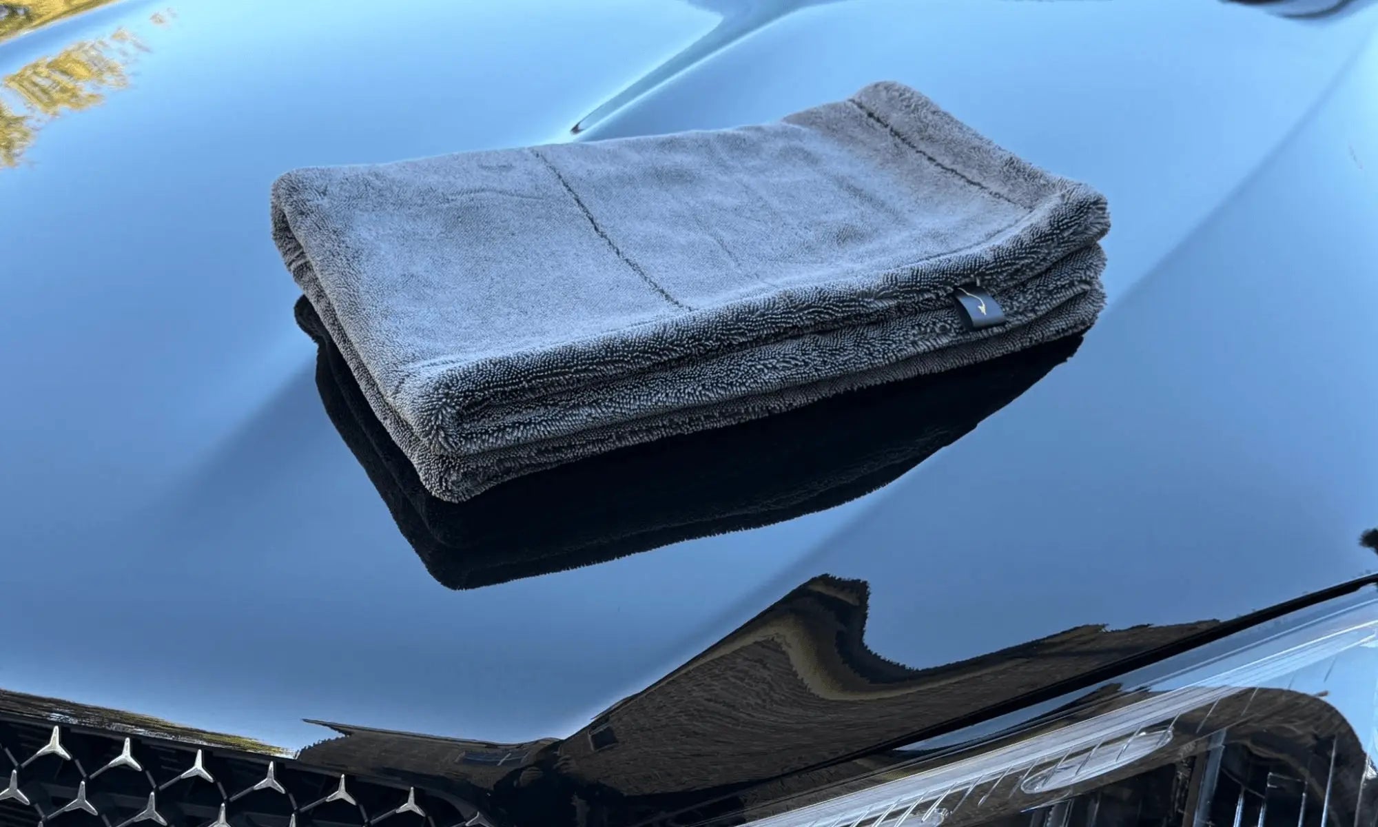 Sleek Max Dry 2K microfiber car drying towel on glossy black hood with reflection