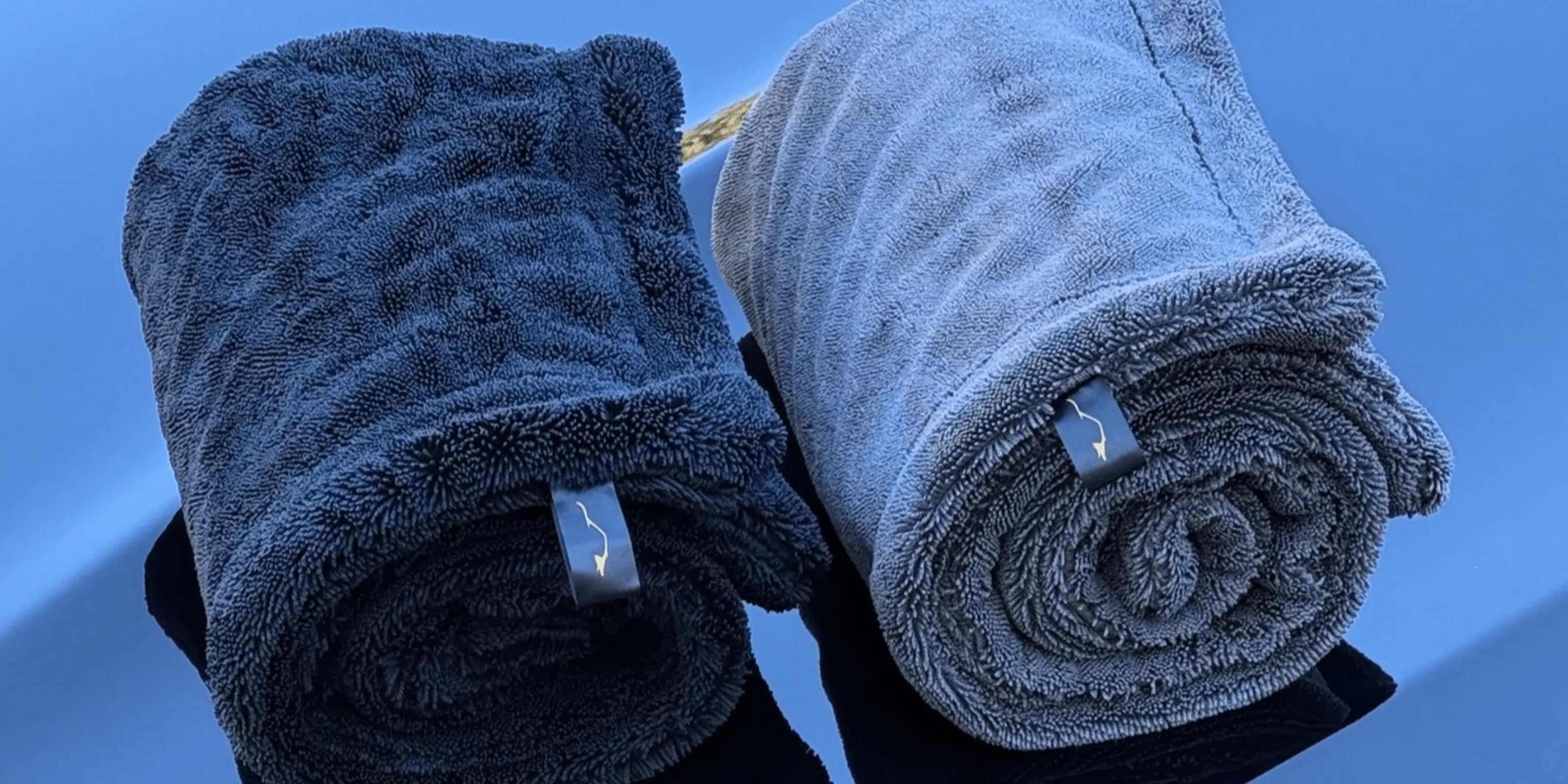 Two rolled-up towels, one black and one gray, on a stand against a black car hood background.